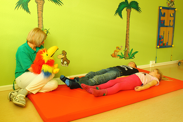 Kinder liegen auf einer Matte, Therapeutin hat Puppe in der Hand